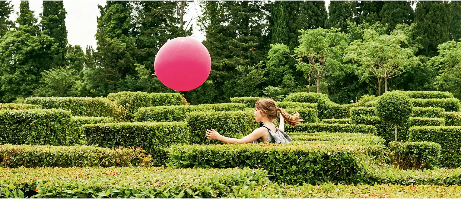 Ein kleines Mädchen rennt einem magentafarbenen Luftballon in einem Irrgarten nach (Foto)