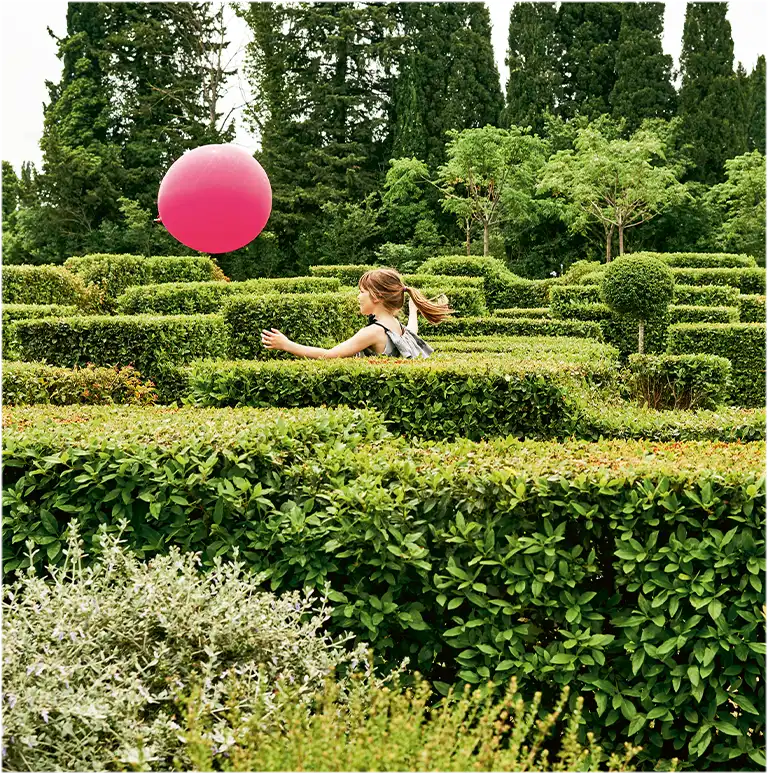 Ein kleines Mädchen rennt einem magentafarbenen Luftballon in einem Irrgarten nach (Foto)